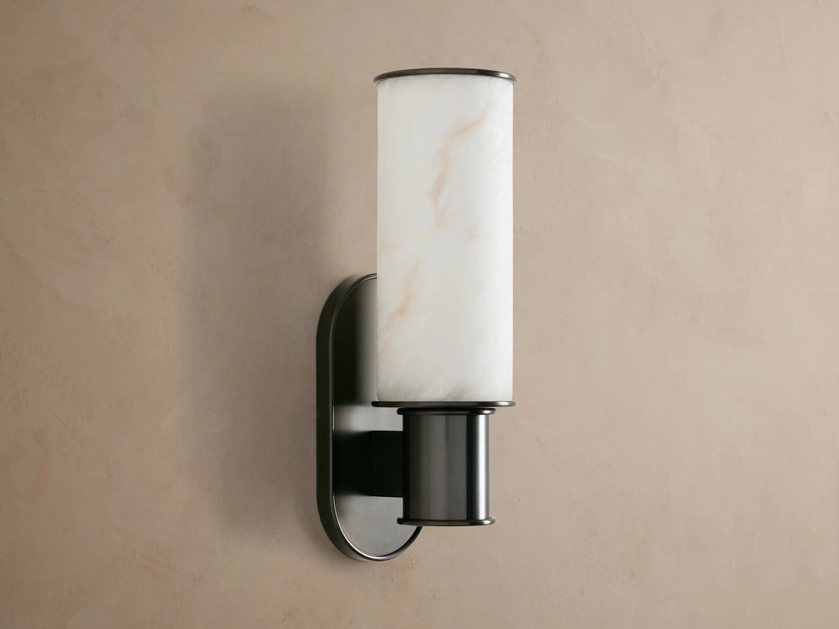 Harlin Sconce: glowing, veined alabaster cylindrical cloche, dark bronze oval backplate on a light wall.