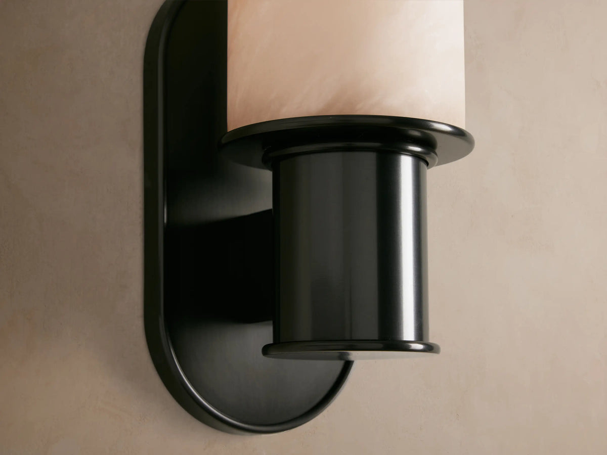 Harlin Sconce mounted vertically; features a white cylindrical alabaster cloche with subtle veining and a dark bronze metal base.