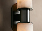 Harlin Double Sconce featuring two stacked alabaster cloches with natural veining on a vertical dark bronze backplate, on a tan wall.