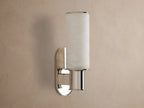 Harlin Sconce: vertical glowing alabaster cylinder, polished nickel racetrack backplate and base, mounted on a neutral wall.