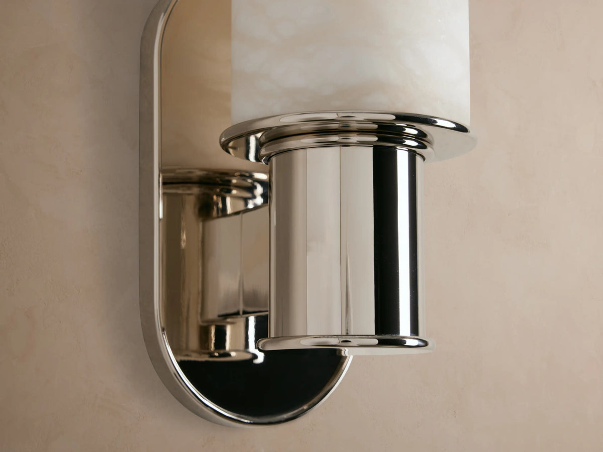 Vertical Harlin Sconce with cylindrical white marbled alabaster cloche and polished nickel base mounted on a beige wall.