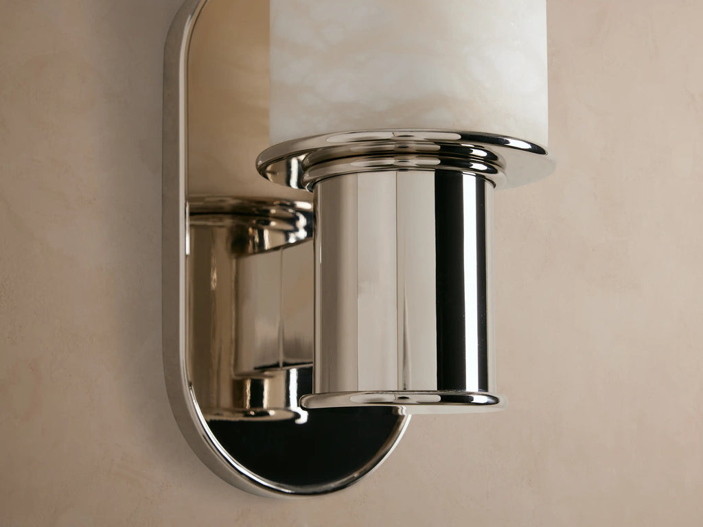 Vertical Harlin Sconce with cylindrical white marbled alabaster cloche and polished nickel base mounted on a beige wall.
