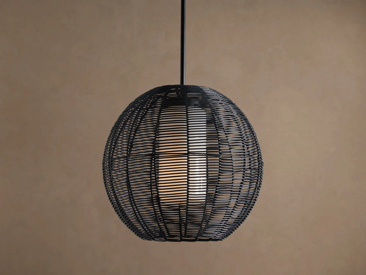 Cohen Globe Outdoor Pendant: Black woven wicker globe with an illuminated white inner shade, hanging from a dark pole against a brown wall.