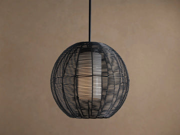 Cohen Globe Outdoor Pendant: Black woven wicker globe with an illuminated white inner shade, hanging from a dark pole against a brown wall.