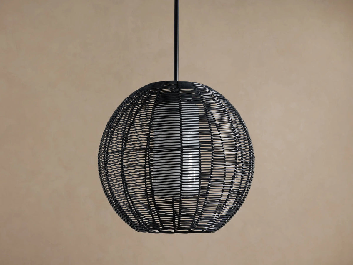 Cohen Globe Outdoor Pendant: Black woven wicker globe with an illuminated white inner shade, hanging from a dark pole against a brown wall.