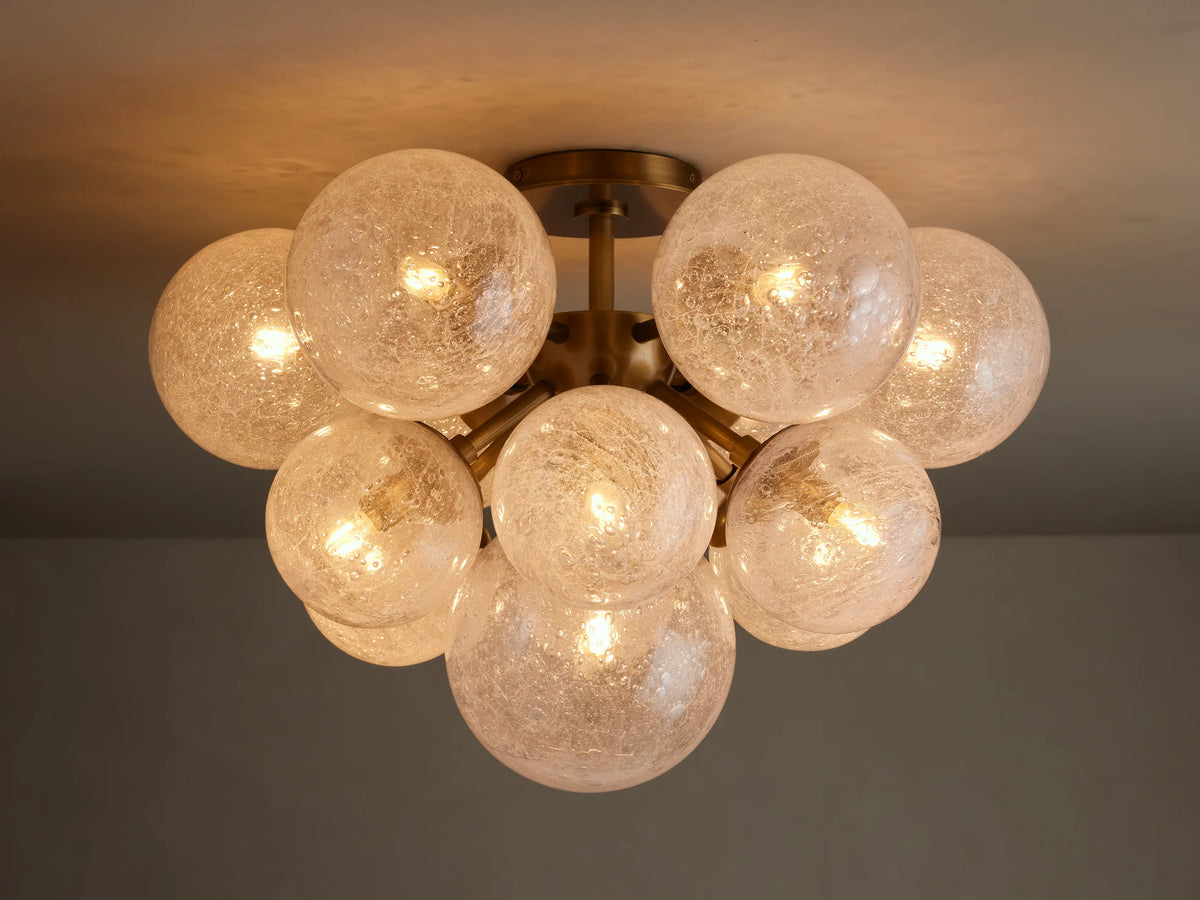 Mandoza Flush Mount, burnished brass base with multiple glowing, textured glass globes clustered on a light ceiling.