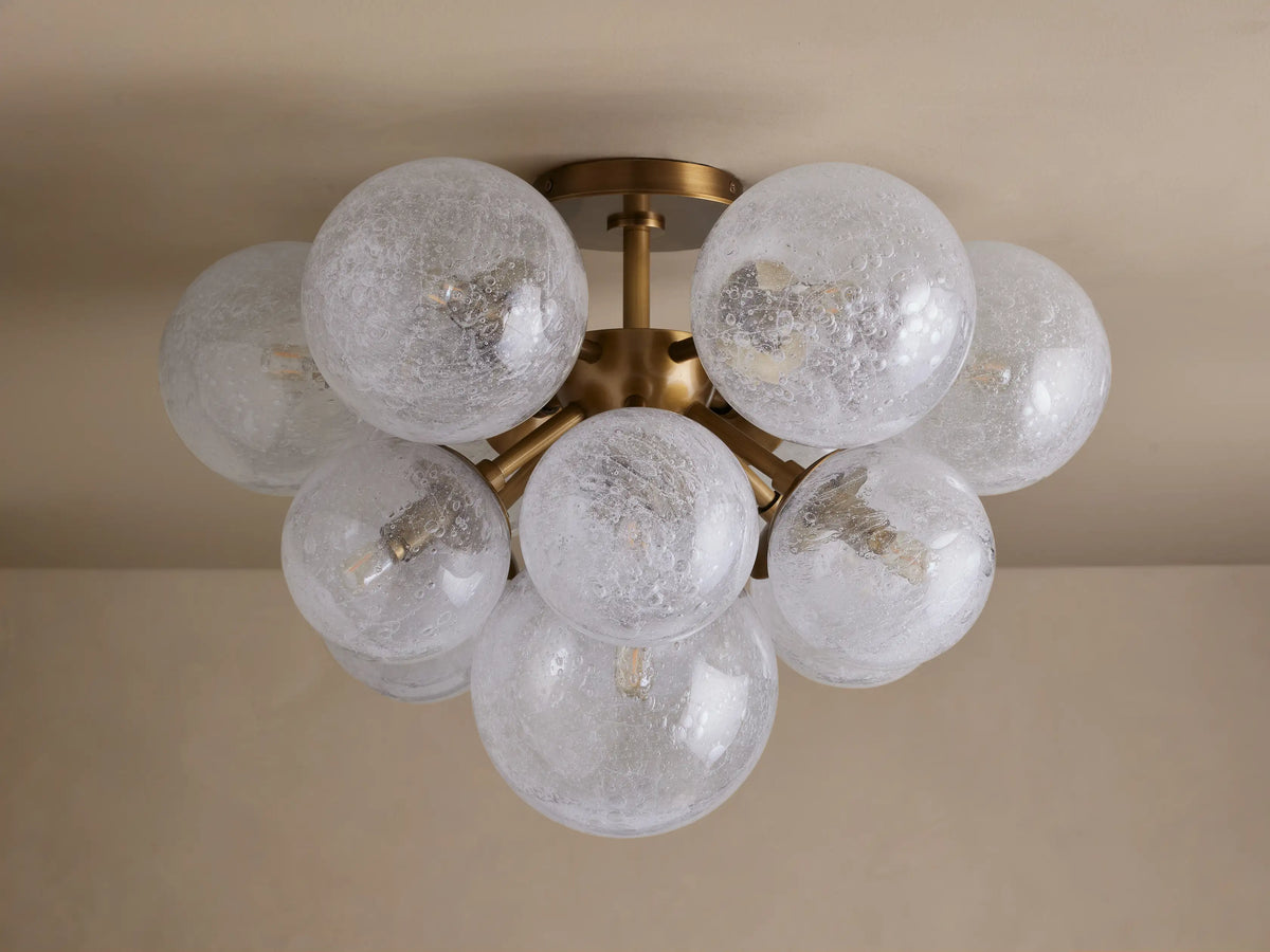 Mandoza Flush Mount, burnished brass base with multiple glowing, textured glass globes clustered on a light ceiling.