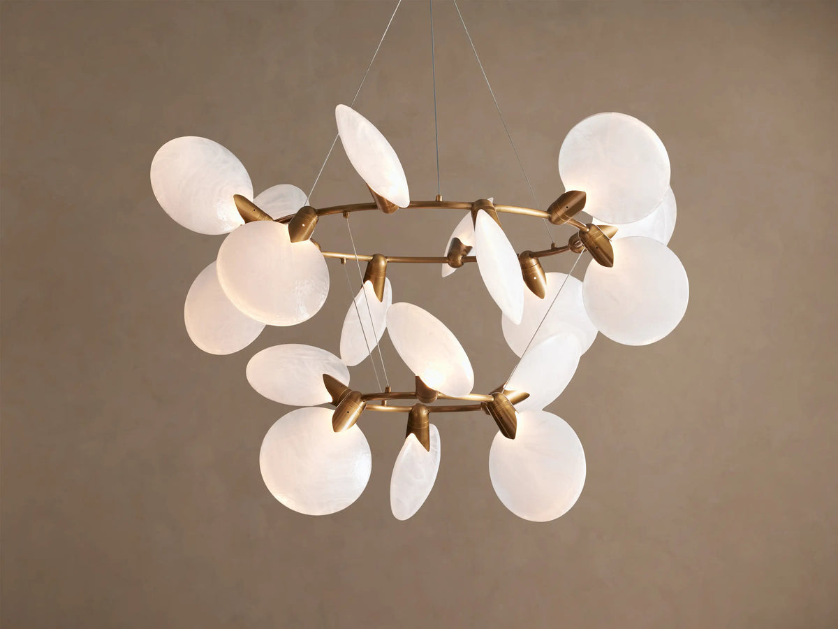 Lyla Chandelier: Modern gold brass chandelier with multiple illuminated circular hand-blown white glass shades, against a plain wall.