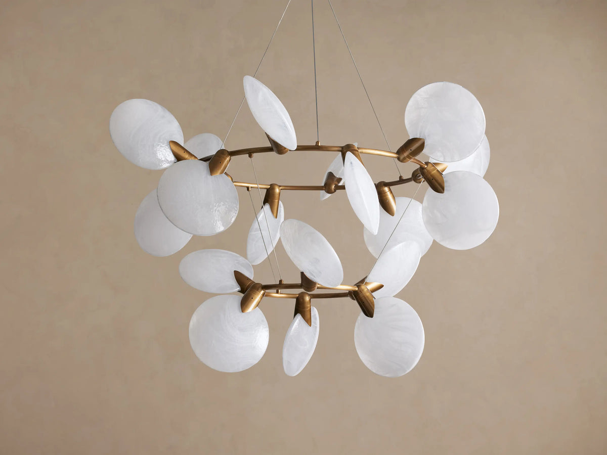 Lyla Chandelier: Modern gold brass chandelier with multiple illuminated circular hand-blown white glass shades, against a plain wall.