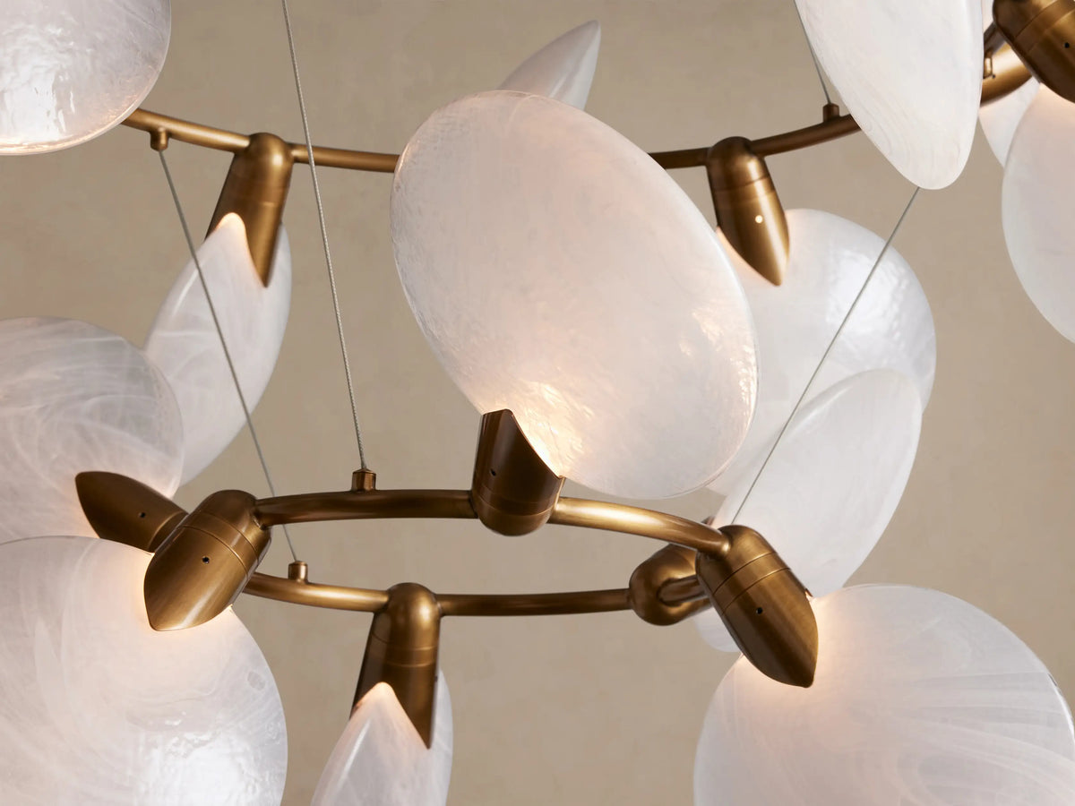 Lyla Chandelier: gold-toned frame with numerous white, textured, hand-blown glass discs in a layered design, suspended.