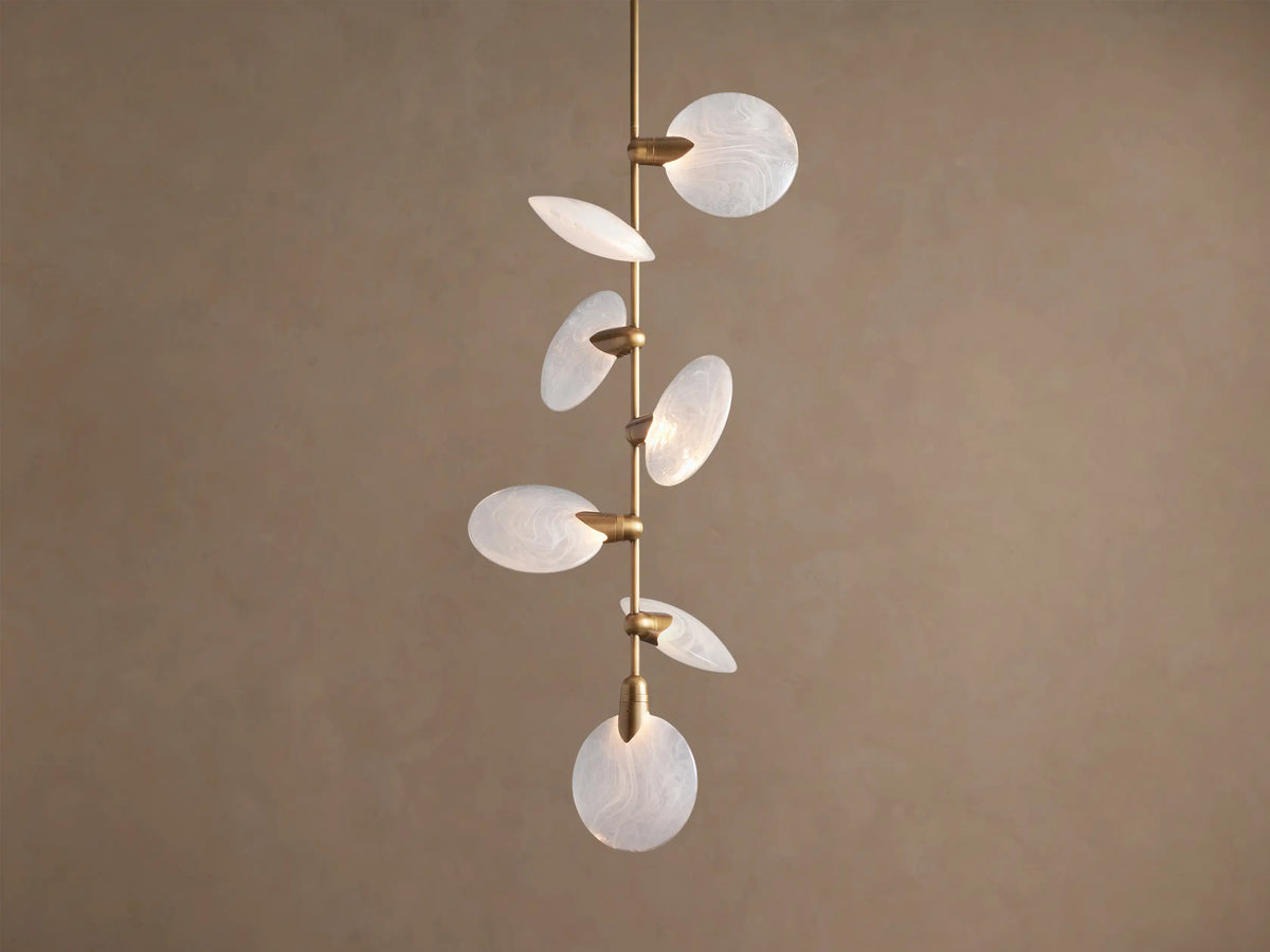 Lyla Pendant: 7 round, swirled hand-blown glass shades with glowing LED lights on a vertical brass stem against a brown wall.