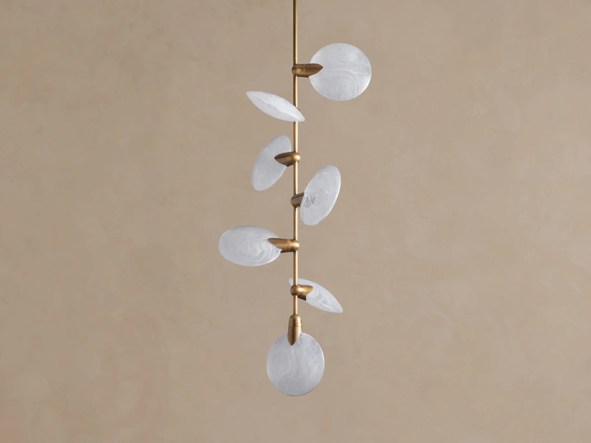 Lyla Pendant: 7 round, swirled hand-blown glass shades with glowing LED lights on a vertical brass stem against a brown wall.