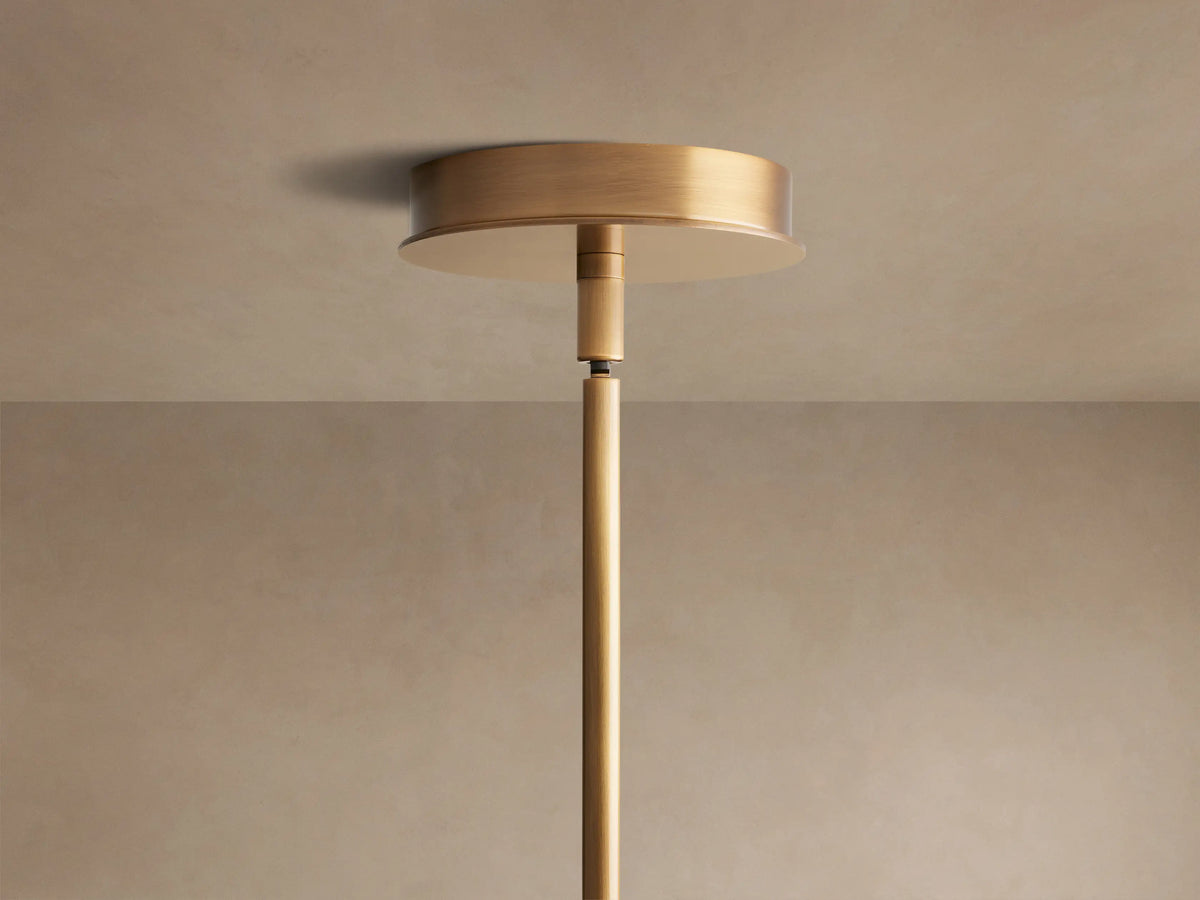 Lyla Pendant, close-up of swirled gray hand-blown glass discs on a vertical brass-plated steel pole against a beige wall.