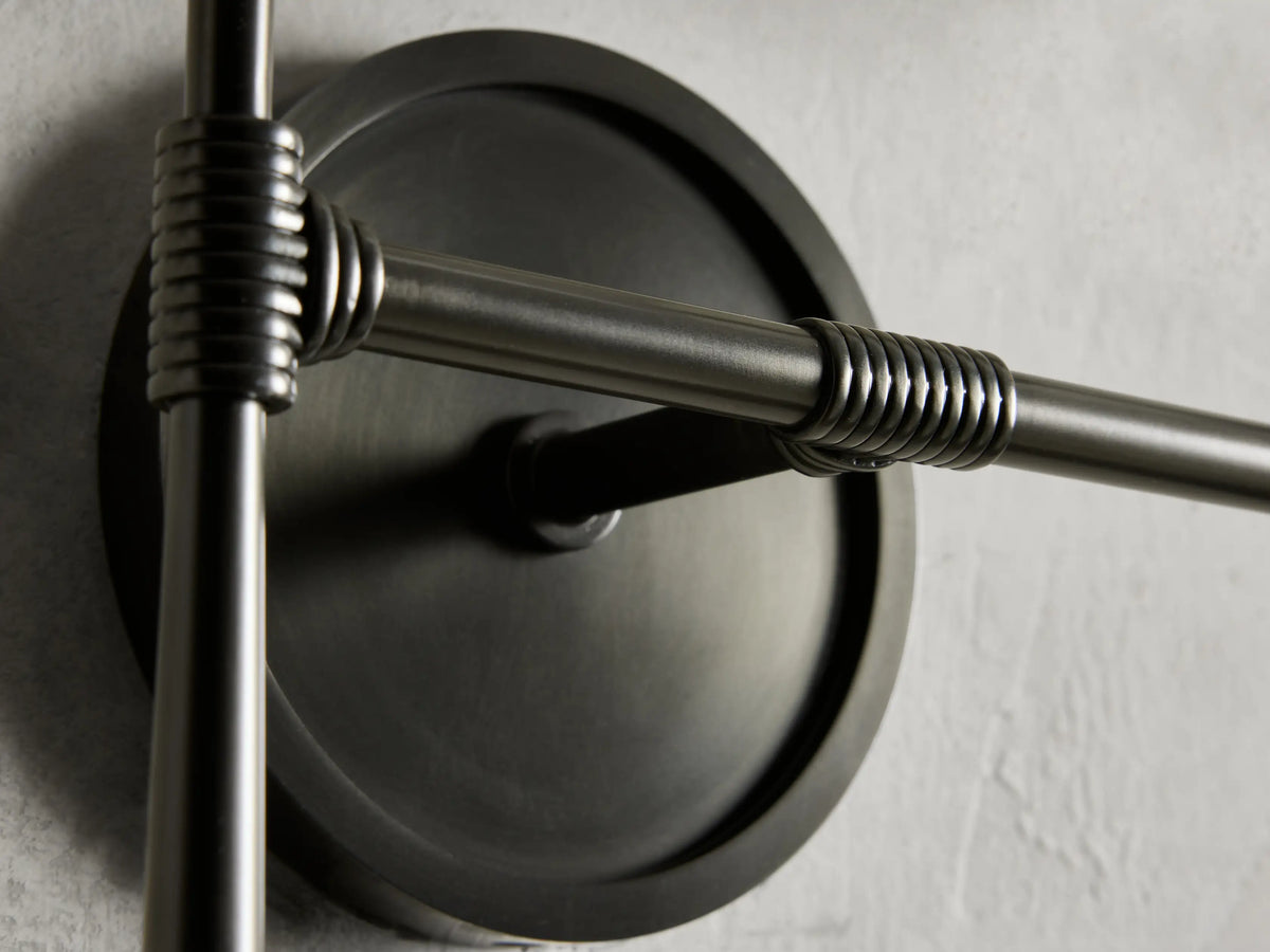 Rhodes Double Sconce with a round, bronze-finished steel backplate and detailed rod design on a textured wall surface.