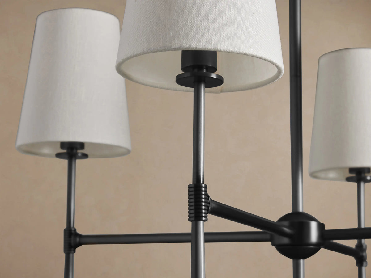 Rhodes Chandelier with 8 tapered light linen shades on a dark bronze-toned metal frame, suspended against a beige wall.