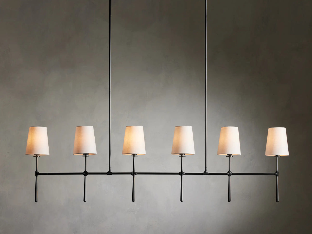 Rhodes Linear Chandelier with six tapered linen shades on a bronze-plated steel frame, suspended against a neutral wall.