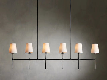 Rhodes Linear Chandelier with six tapered linen shades on a bronze-plated steel frame, suspended against a neutral wall.