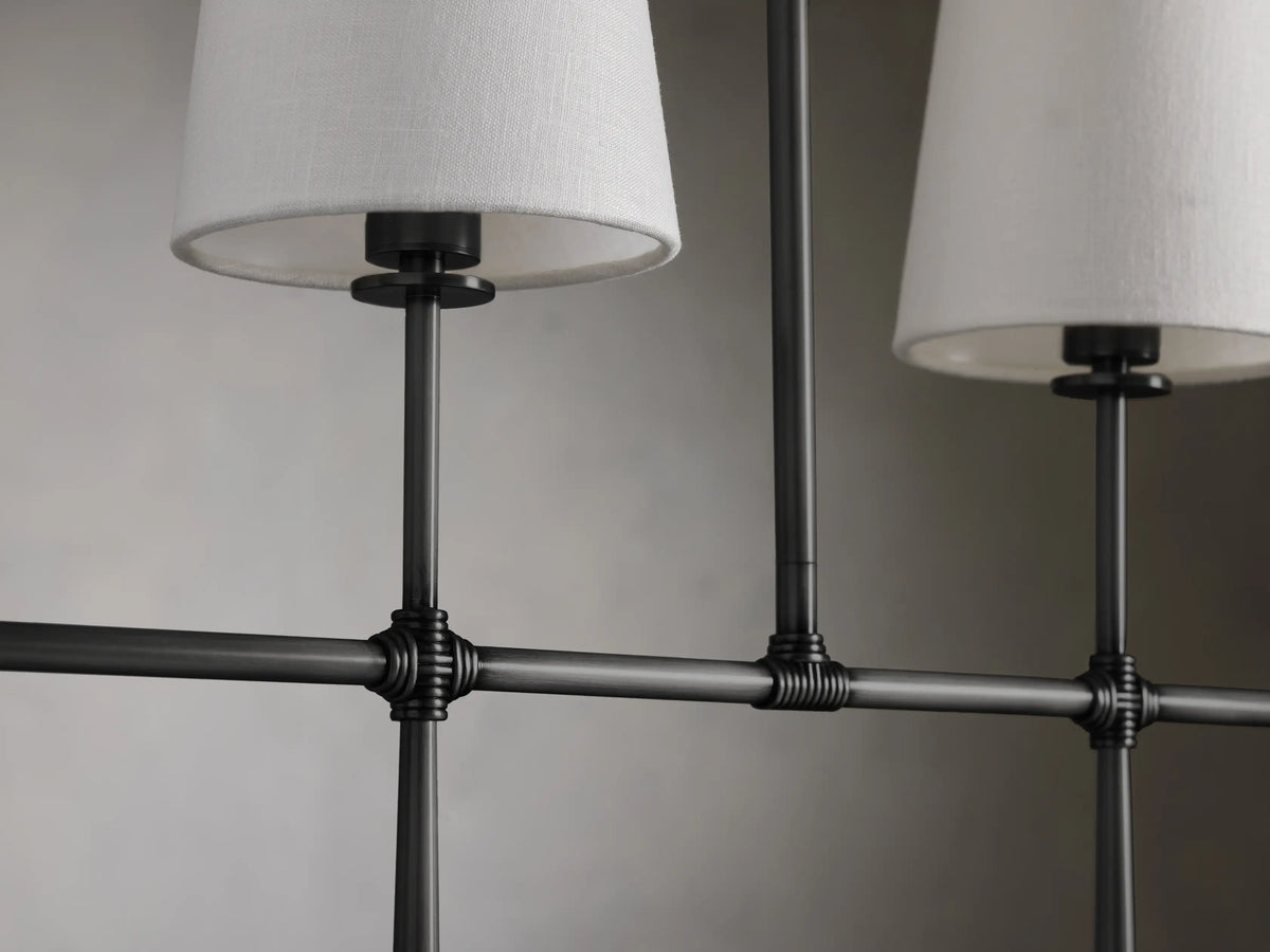 Rhodes Linear Chandelier with black steel frame, six white tapered linen shades, set against a gray wall.