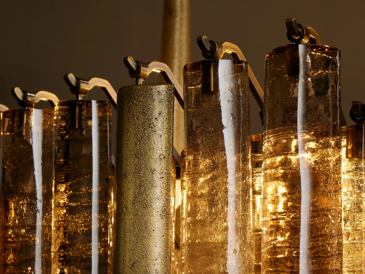 Close-up of Neve Linear Chandelier's warm glowing bronze cast glass cylinders and textured champagne-finished aluminum.