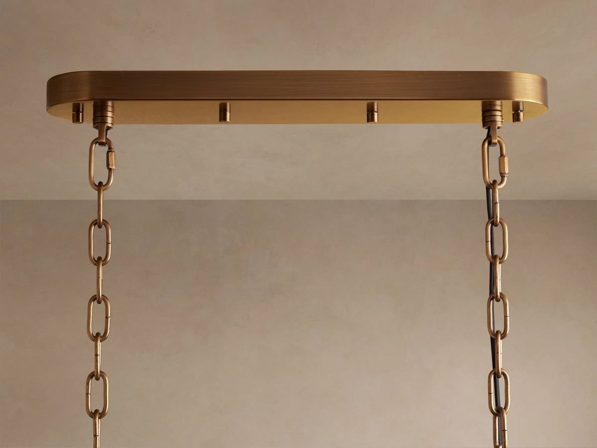 Neve Linear Chandelier. Close-up of an oval brass ceiling plate with two brass chains hanging down against a light-colored ceiling.