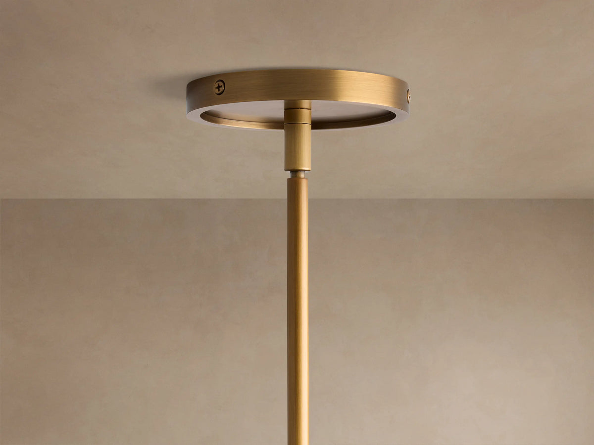 Close-up of Rhodes Round Chandelier with burnished brass arms, ribbed connector, and white tapered linen shades against a light wall.