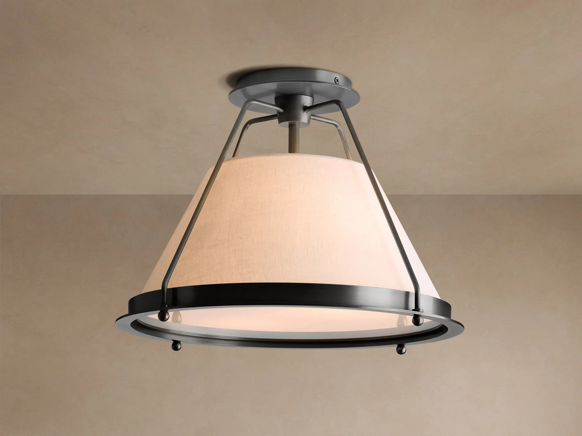 Shelton Flush Mount ceiling light with dark metal frame and large, tapered cream linen shade glowing warmly, mounted on a beige ceiling.