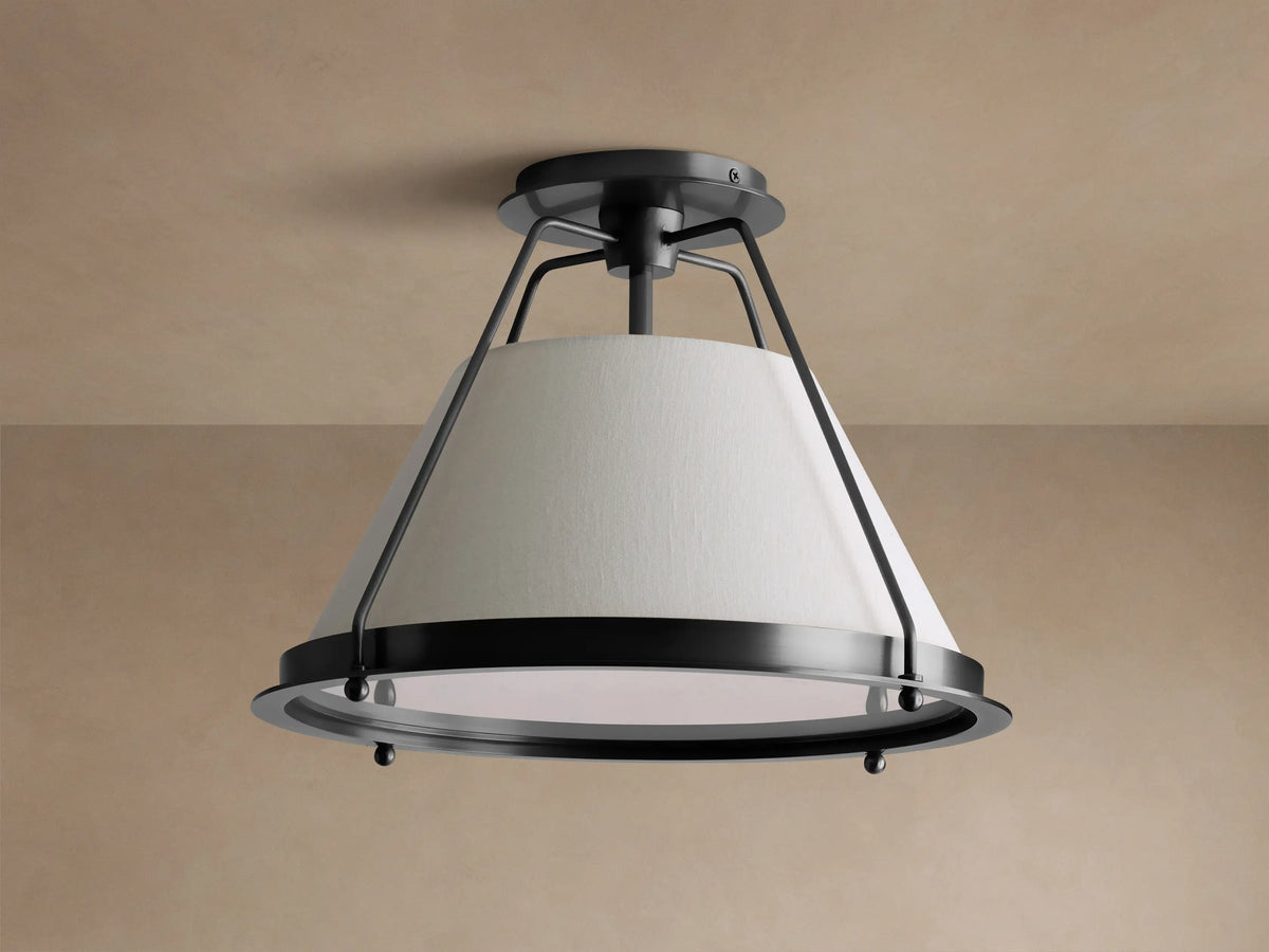 Shelton Flush Mount ceiling light with dark metal frame and large, tapered cream linen shade glowing warmly, mounted on a beige ceiling.