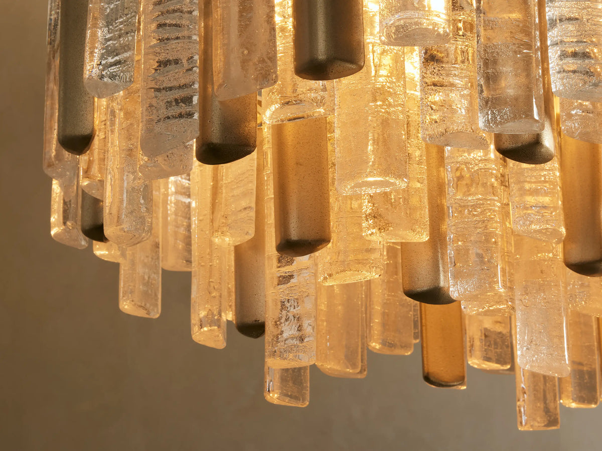 Neve Linear Chandelier close-up: clear & bronze textured cast glass rods, warmly glowing from brass-finished tops.