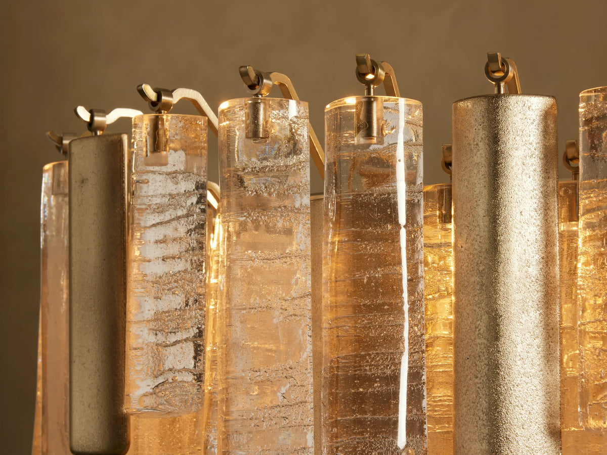 Close-up of Neve Linear Chandelier with warm glowing, textured clear and bronze cast glass elements alongside champagne aluminum.