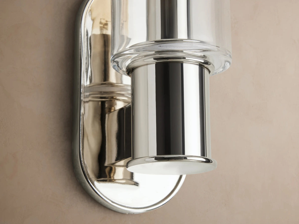 Harlin Clear Sconce, polished nickel, clear glass cloche with a long filament bulb, mounted vertically on a beige wall.