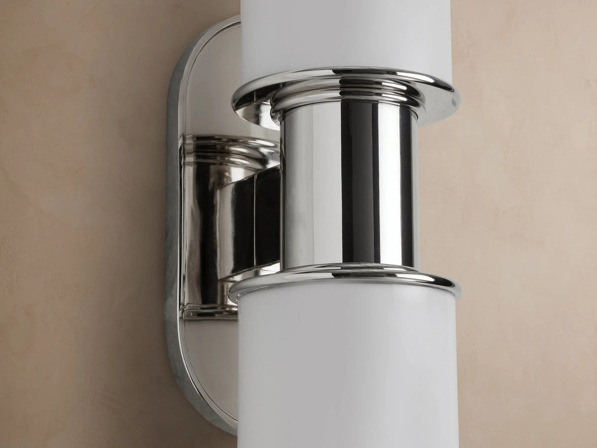 Harlin Double Sconce, vertically mounted, features two white milk glass cylinders and polished nickel accents on a beige wall.