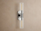 Vertical Harlin Double Sconce with polished nickel finish and two clear glass cloches revealing illuminated Edison bulbs on a brown wall.