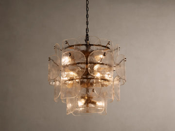 Blaire Round Chandelier with layered, curved clear glass panels creating a textured effect. Lit with warm light, hung by a brass-finished chain.