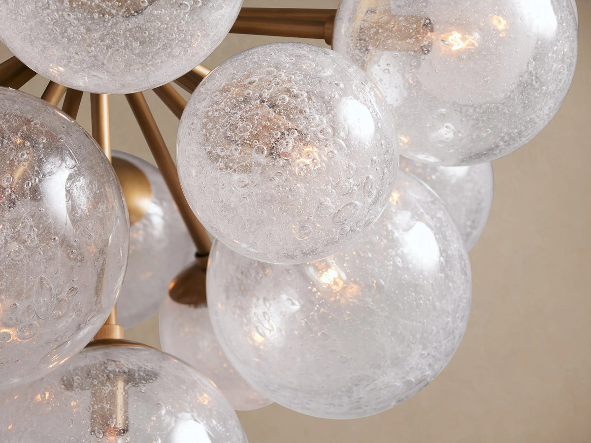 Mandoza Chandelier: Clear and frosted hand-blown glass globes on burnished brass arms, suspended against a light tan background.