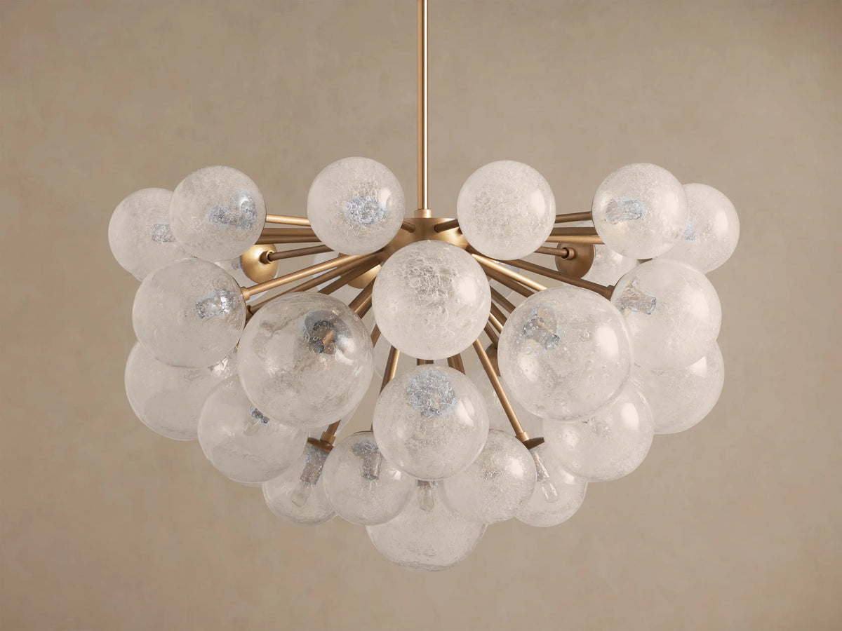 Mandoza Chandelier with a gold-toned frame and many illuminated, textured glass globes against a light brown wall.