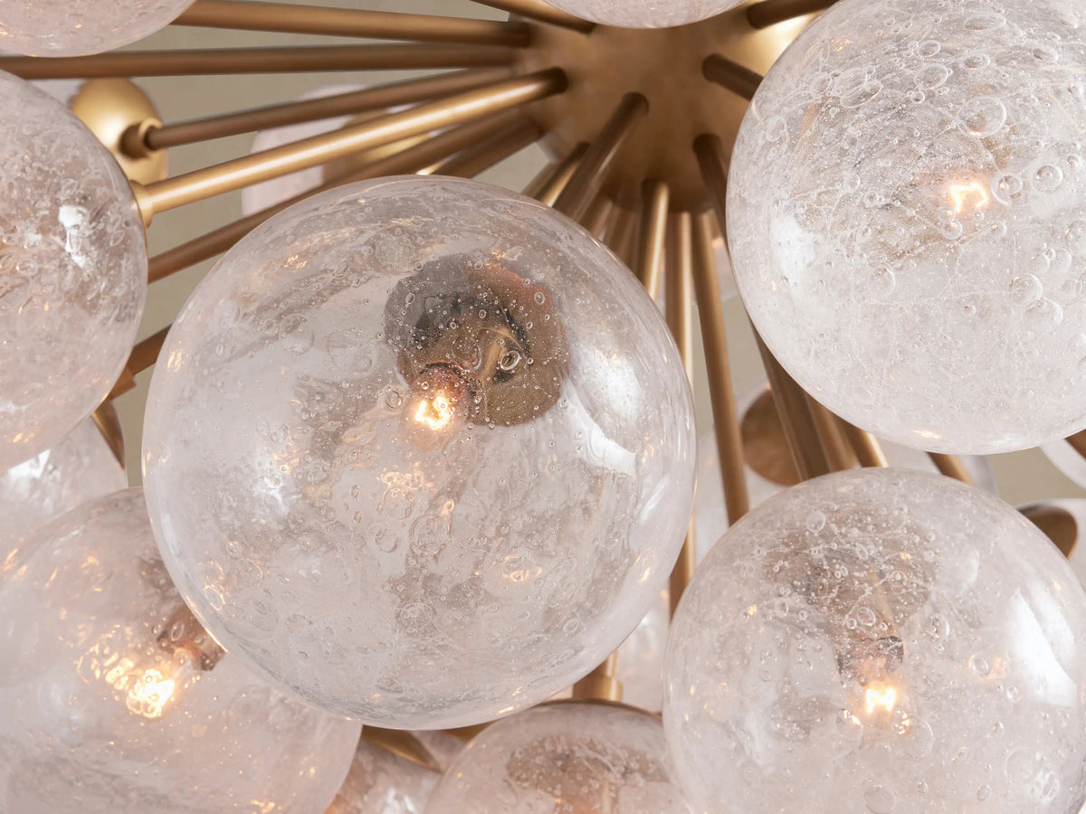 Mandoza Chandelier, a modern starburst-style fixture with burnished brass arms and numerous textured, clear glass globes.