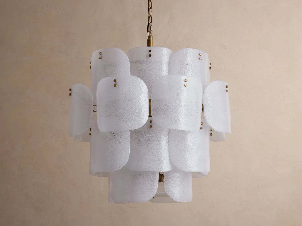 Blaire Round Chandelier with layered, curved white pearlescent glass panels and brass accents, hanging against a light wall.