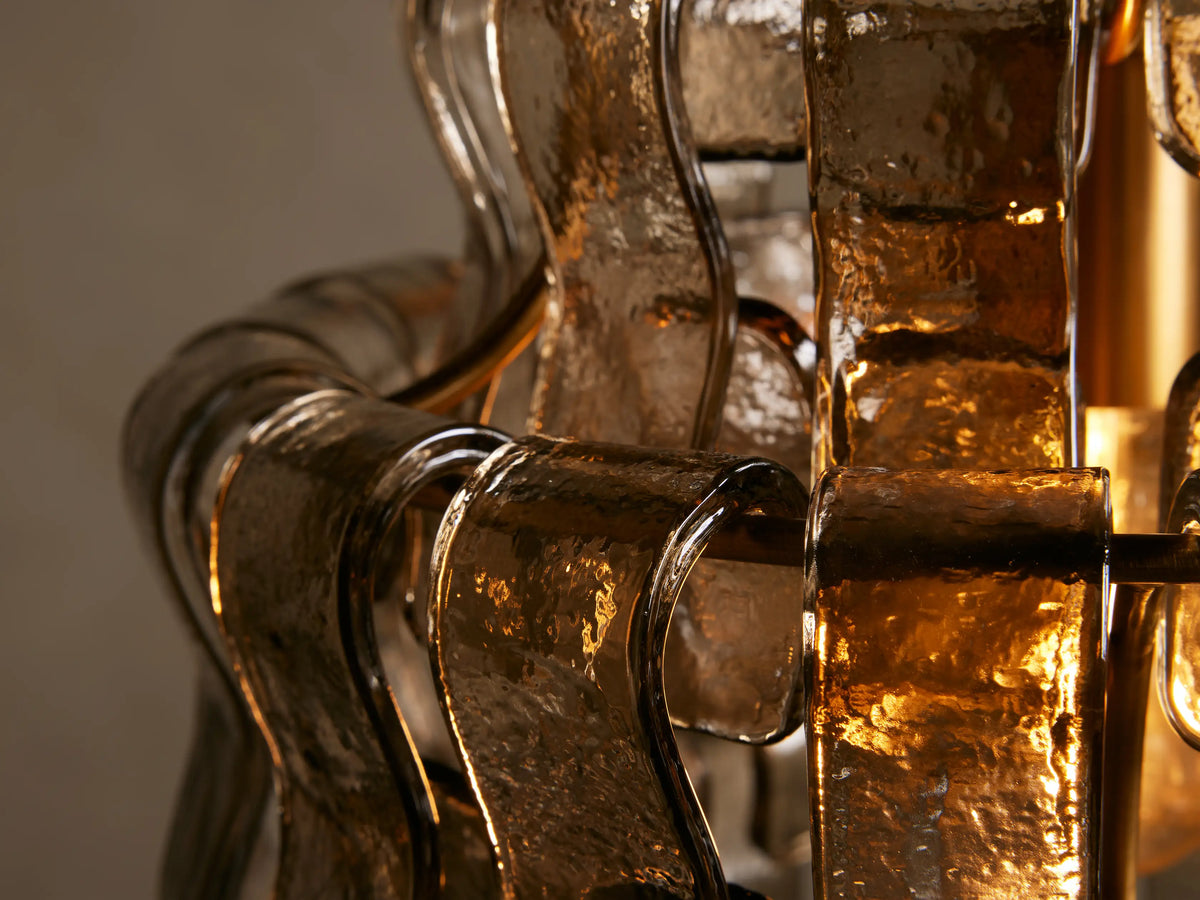 Ghiaccio Pendant with curved glass and steel frame, showing a tiered, wave-like design. Hangs from a gold rod and chain.