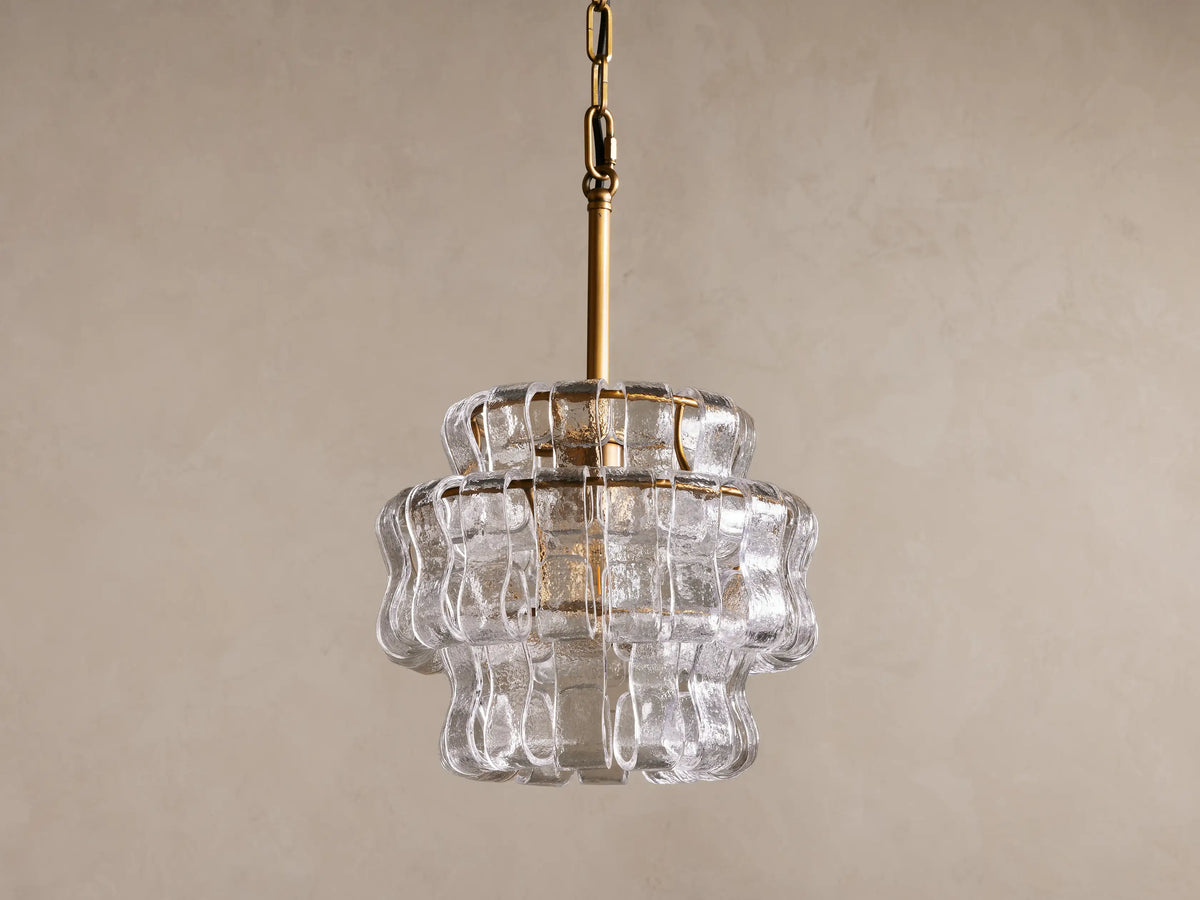 Ghiaccio Pendant with layered, curved glass design, hanging from a bronze rod with black chain; light illuminating from within.