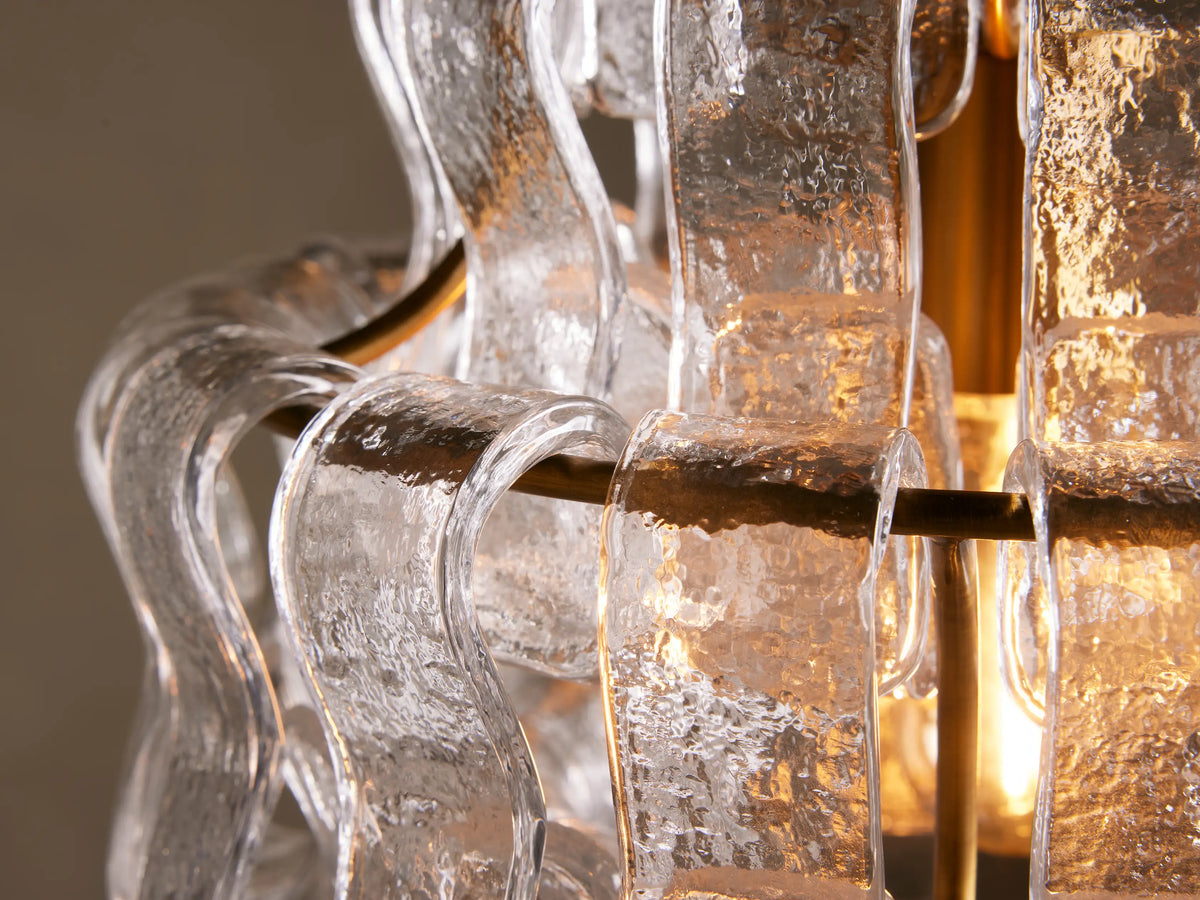 Ghiaccio Pendant with curved glass design and steel accents, featuring a layered, wave-like structure. Hangs from a brass rod.