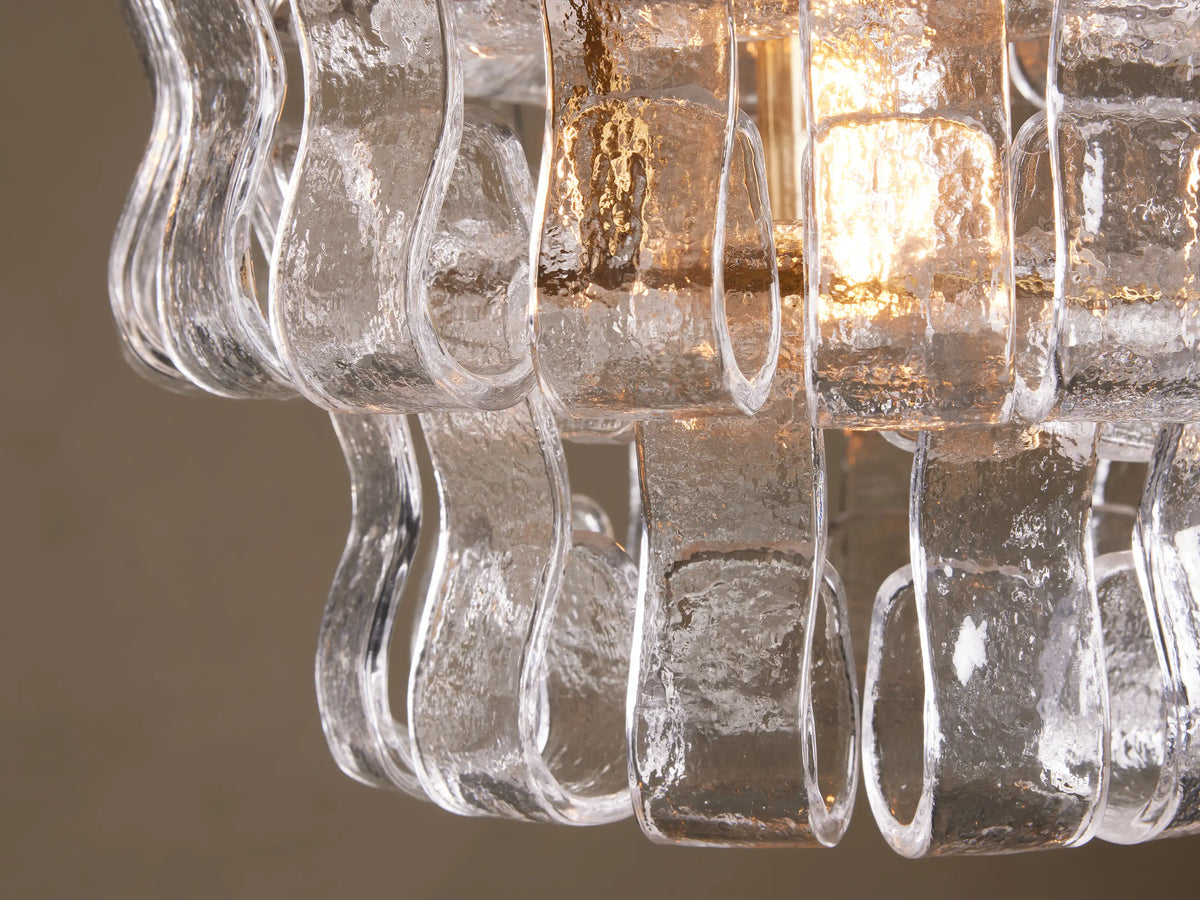 Curved glass strands of the Ghiaccio Pendant form a textured, wavy design around the warm glow of a bulb, mounted on a steel frame.