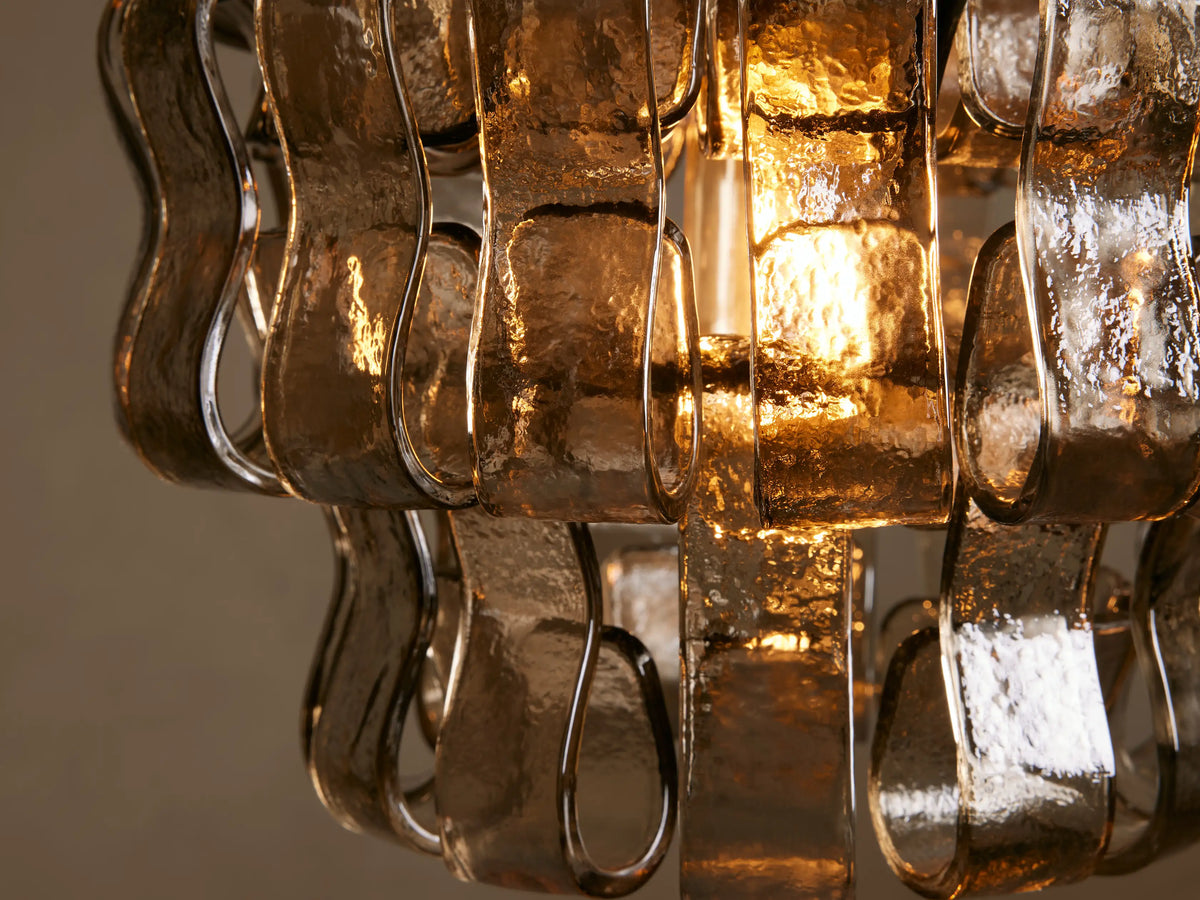 Close-up of the Ghiaccio Pendant, showcasing interwoven, curved glass ribbons with a golden glow from the light inside.