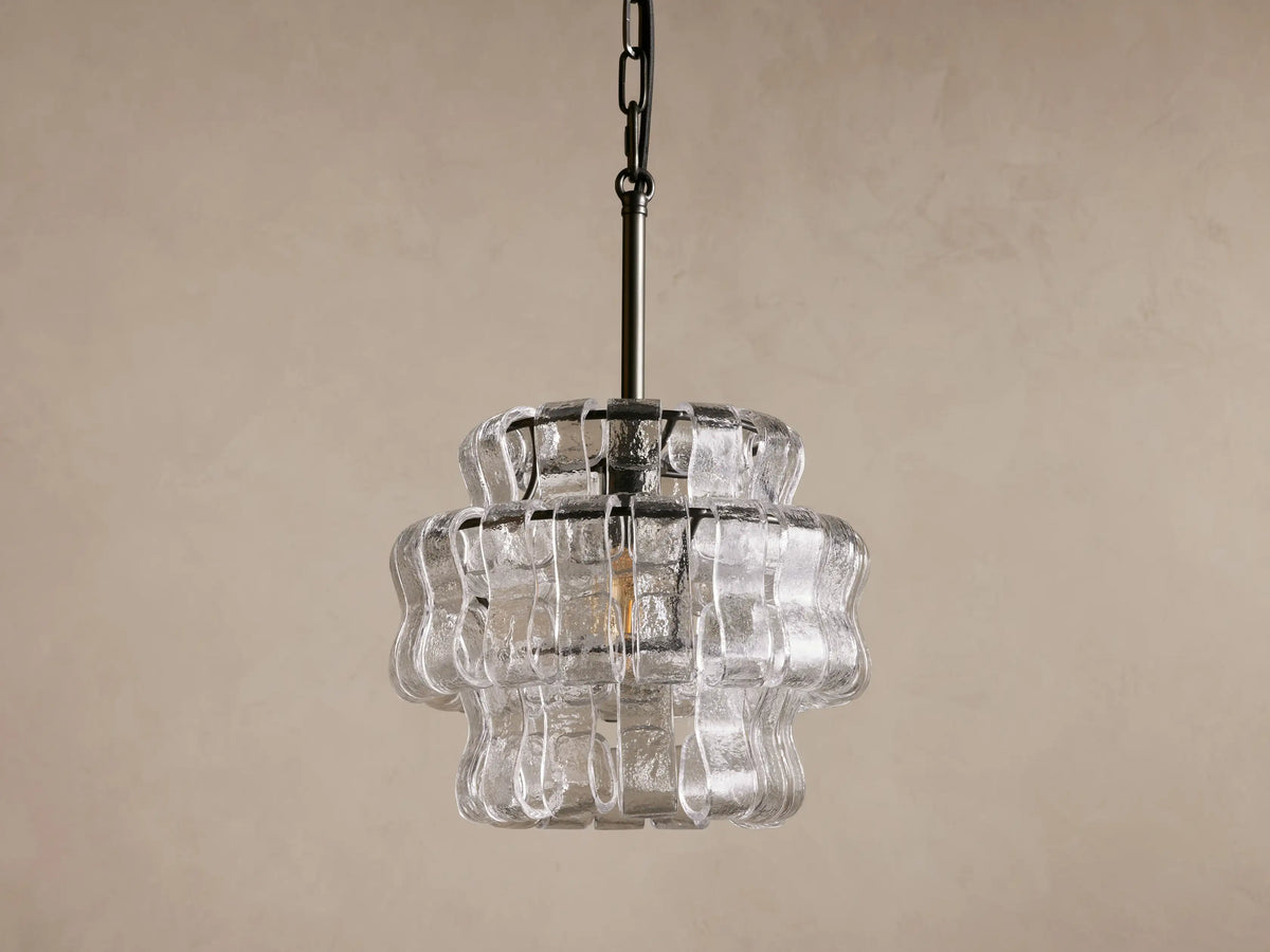Pendant light with curved glass design, emitting warm light. Steel chain and black cord visible, set against a plain background.