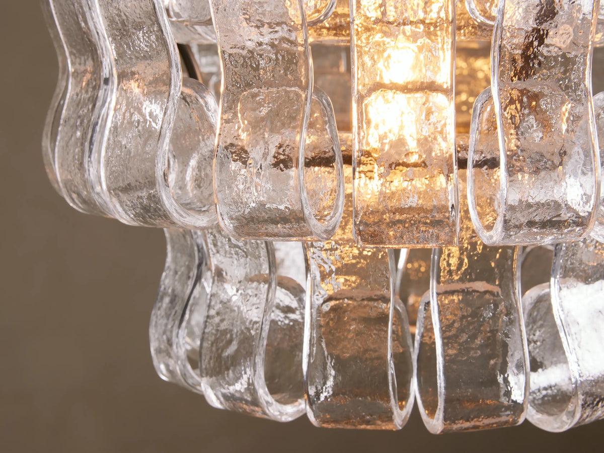 Curved glass pieces of the Ghiaccio Pendant with a textured surface, surrounding a glowing bulb, mounted on a metal frame.