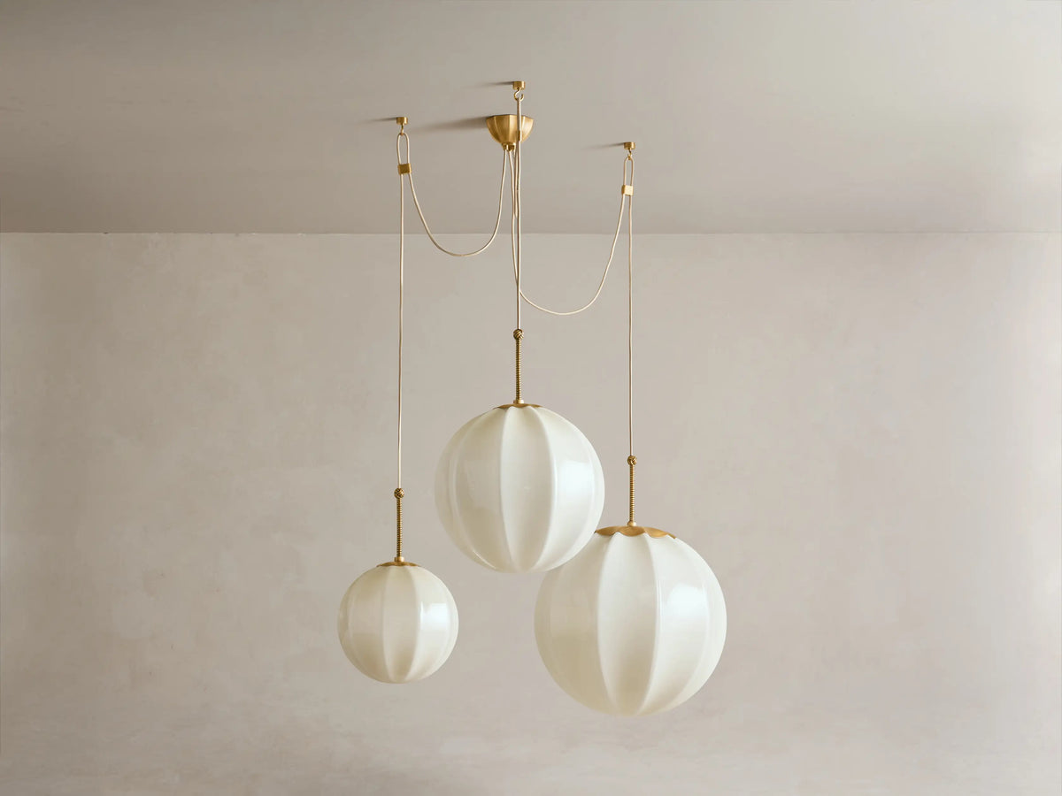 Agnes Chandelier with three cream, paneled glass globes suspended by antique brass hardware in a draped arrangement.