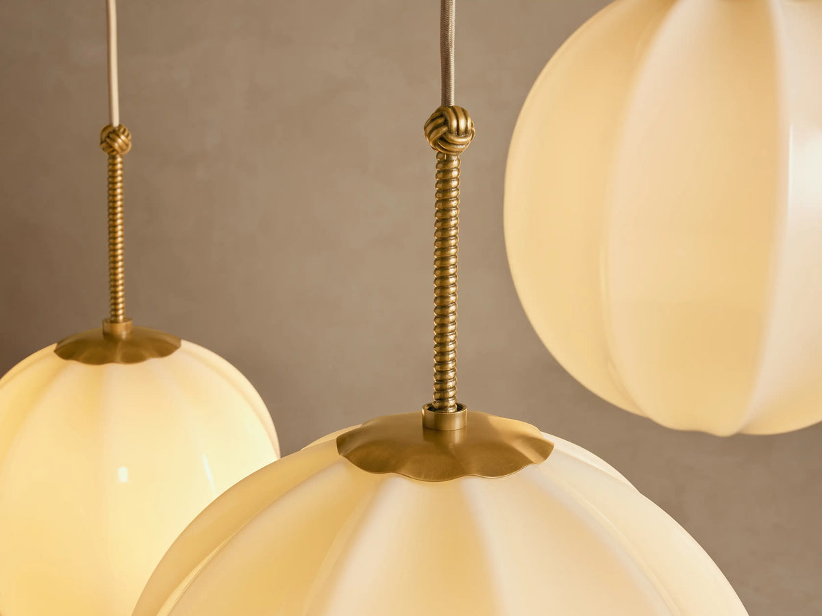 Agnes Chandelier featuring three cream paneled glass globes in varying sizes, suspended by antique brass hardware from the ceiling.