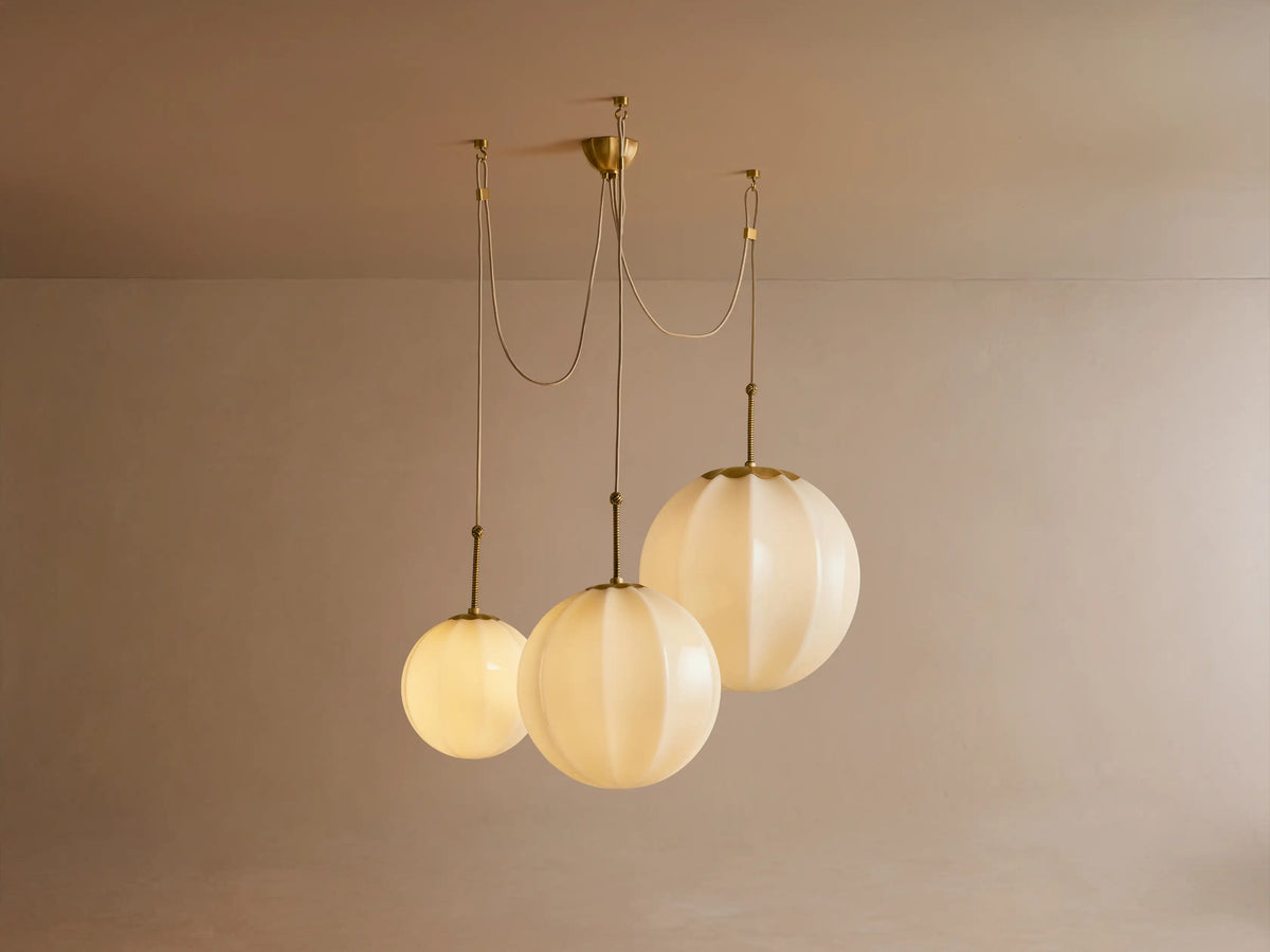 Close-up of Agnes Chandelier: Cream paneled glass globes glow softly, suspended by antique brass rods with knotted detail.