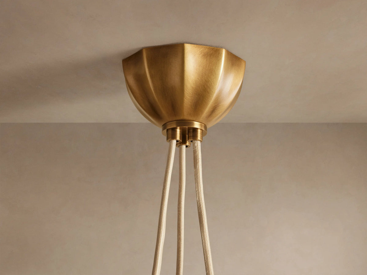 Agnes Chandelier: Three cream paneled glass globes glowing, suspended by antique brass hardware in a draped arrangement.