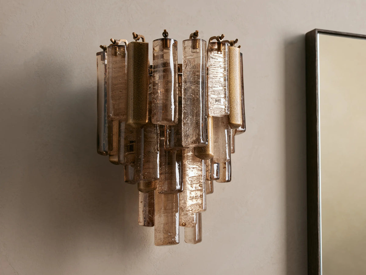 Neve Sconce, crafted from staggered bronze cast glass elements and champagne-finished aluminum, illuminated with a warm glow.