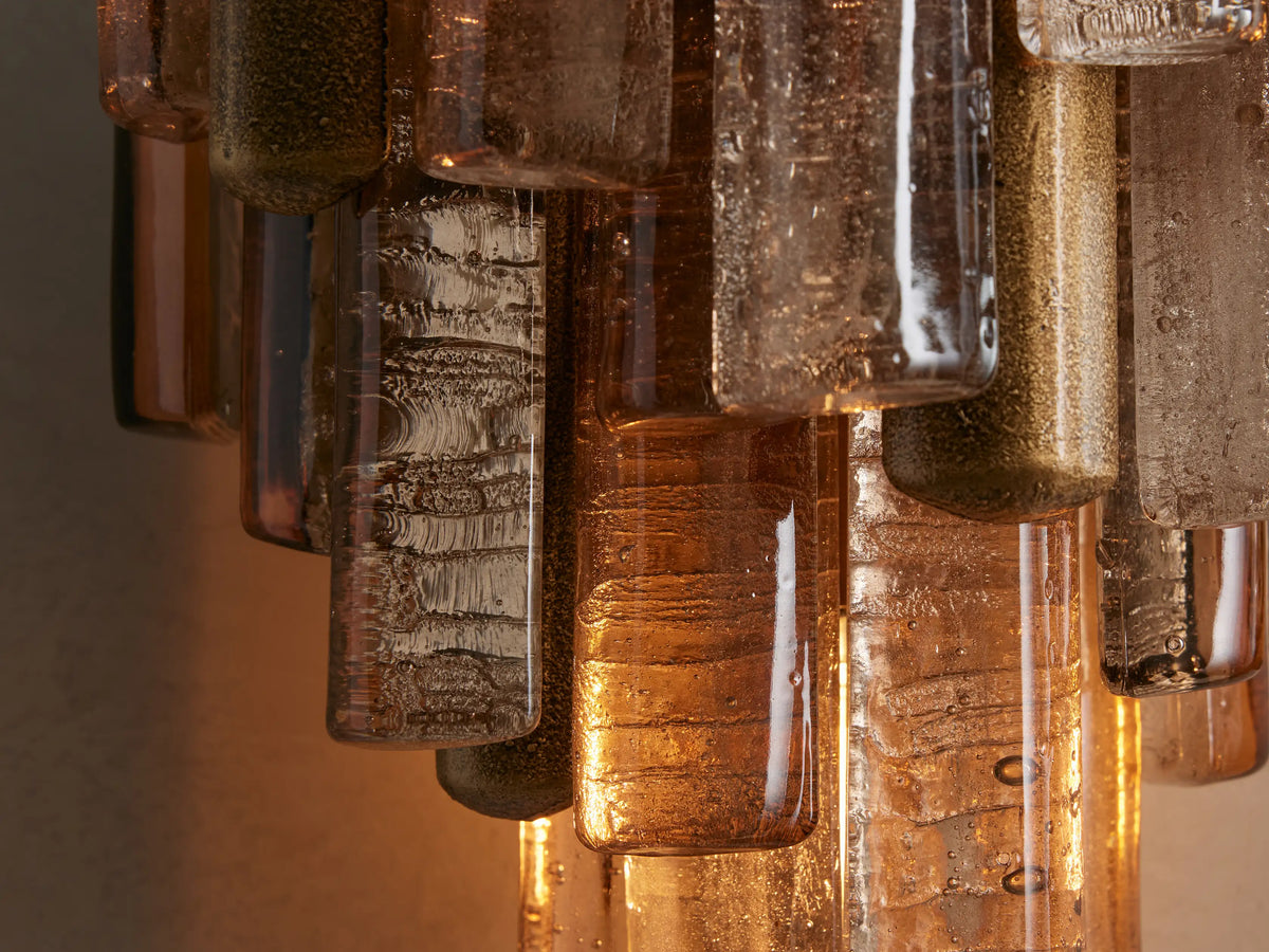 Neve Sconce: Multi-tiered, textured bronze cast glass rods with brass mounts, illuminated, mounted on a neutral wall.